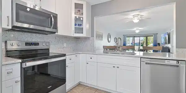 Image 4: Kitchen with appliances with stainless steel finishes, glass insert cabinets, light stone countertops, and white cabinetry