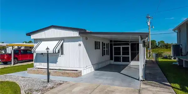 Image 2: White vertical siding exterior with black shutters, a striped window awning, a covered screened-in porch, and a concrete driveway