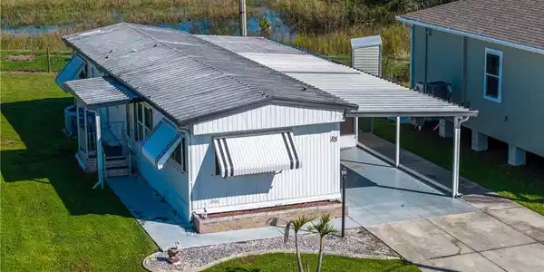 Image 3: White siding exterior with a covered carport, striped window awnings, and an adjacent storage shed