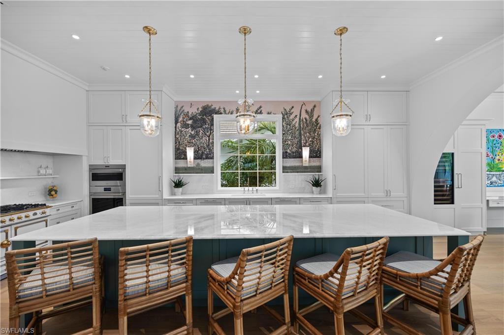 Image 4: Kitchen with a breakfast bar, white cabinets, a spacious island, and decorative light fixtures