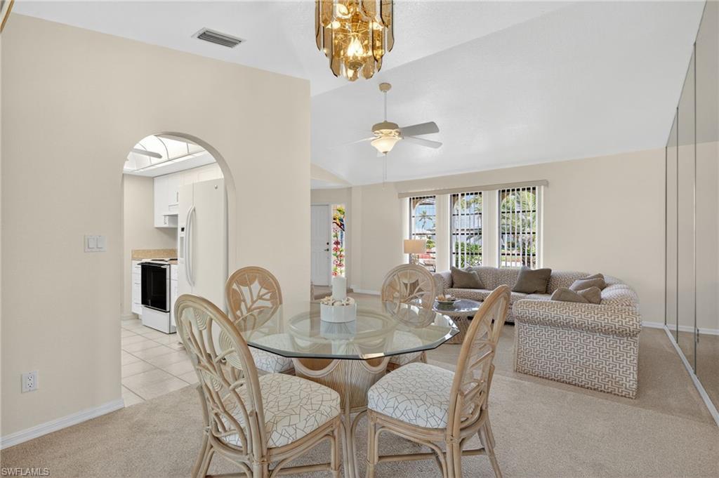 Image 3: Dining space with light colored carpet, lofted ceiling, ceiling fan, arched walkways, and a chandelier