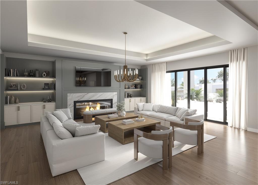 Image 4: Living room with a premium fireplace, wood finished floors, a chandelier, a tray ceiling, and built in shelves