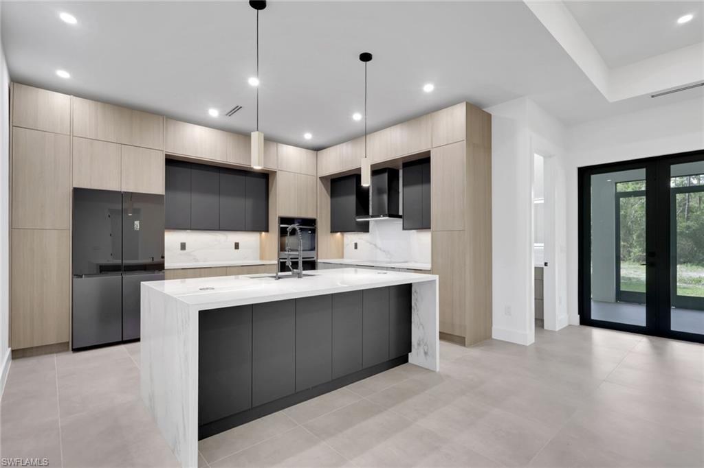 Image 4: Modern kitchen featuring a waterfall island with a light stone countertop, flat-panel cabinetry in a two-tone finish, integrated refrigerator, and built-in wall oven
