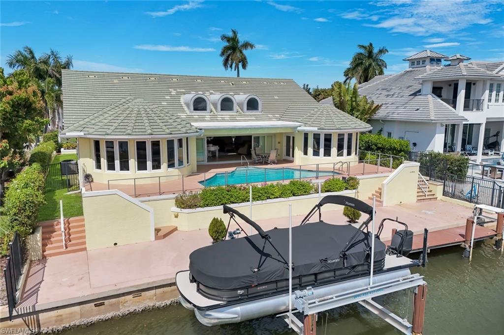 Image 1: Rear view of property featuring a patio area, boat lift, a tiled roof, and a water view