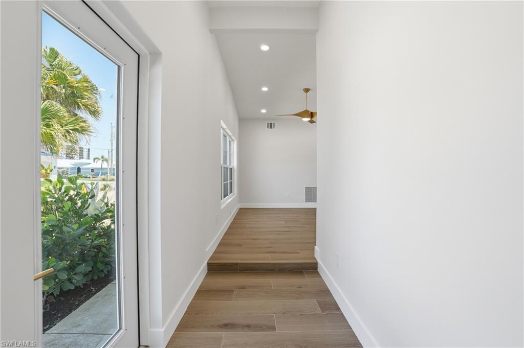 Image 3: Inviting entry with light-toned flooring, crisp white walls, and a large glass-paned door offering natural light and views of tropical foliage - Virtually Edited Image