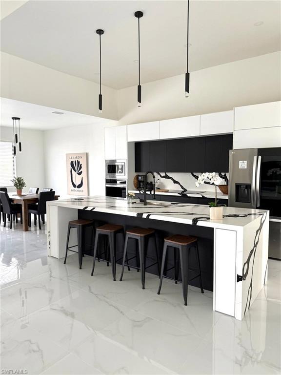 Image 3: Kitchen featuring hanging light fixtures, a large island with sink, light marble finish floors, modern cabinets, and white cabinets