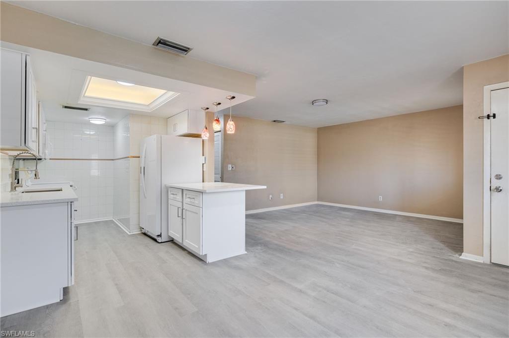 Image 1: Kitchen featuring white cabinetry, light stone counters, open floor plan, freestanding refrigerator, and light wood-style floors