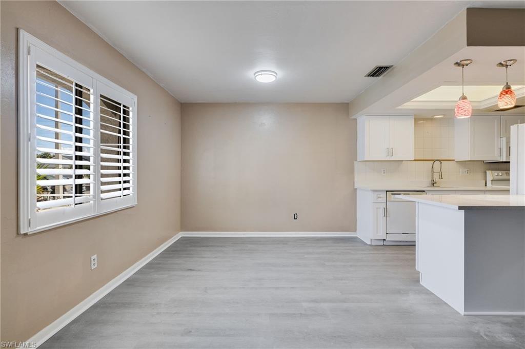 Image 3: Kitchen featuring white cabinets, pendant lighting, light wood finished floors, tasteful backsplash, and white appliances