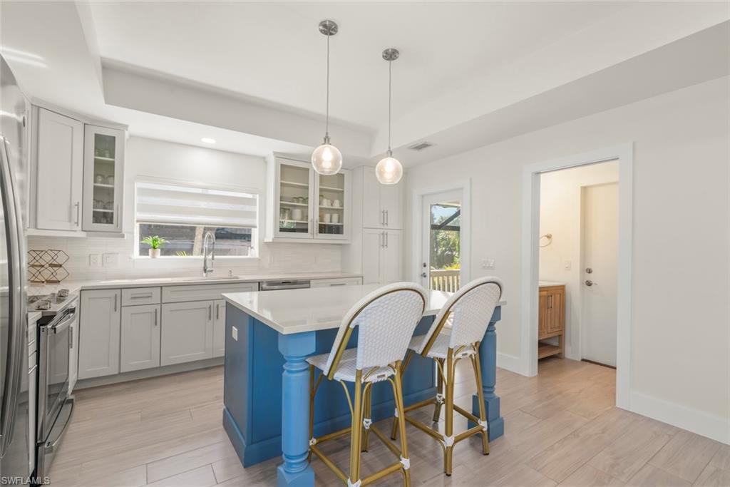 Image 3: Kitchen with light wood-style floors, stainless steel appliances, a breakfast bar area, glass fronted cabinets, and a tray ceiling
