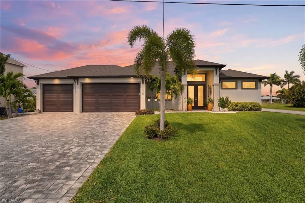 Image 4: Prairie-style home featuring decorative driveway, a garage, soffit lighting, stucco siding, glass doors, and a front lawn