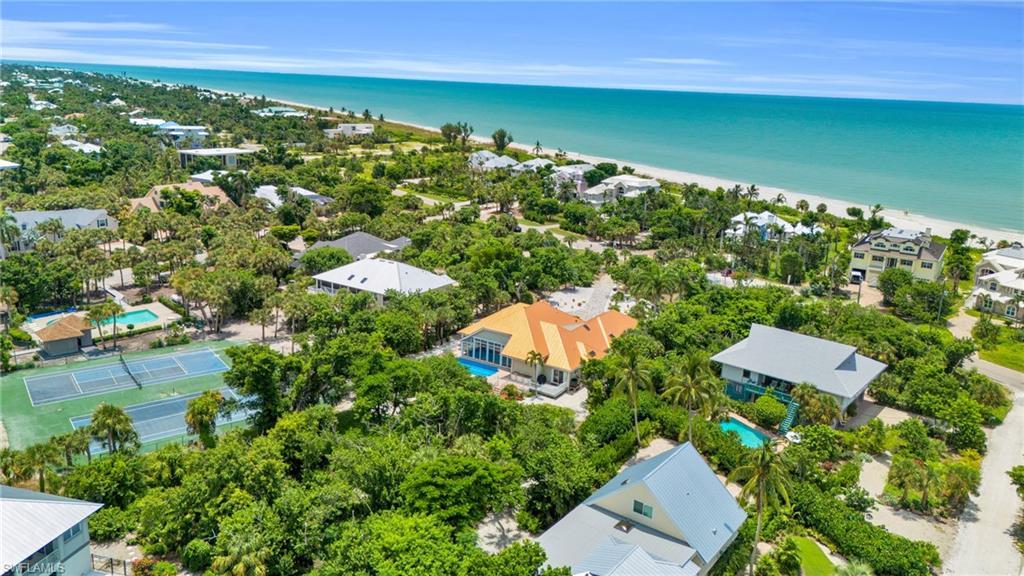 Image 4: Aerial perspective showcasing a coastal community with numerous residences, two tennis courts, and a sandy beachfront bordering turquoise waters