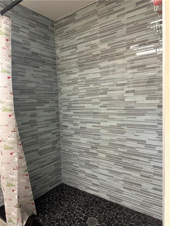Image 3: Shower enclosure featuring linear mosaic wall tile in varying shades of gray, dark pebble-finish flooring, and a visible floor drain
