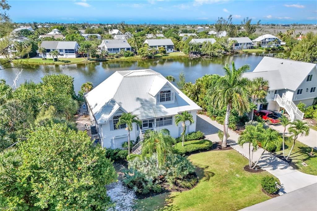 Image 2: Waterfront property featuring a metal roof, mature tropical landscaping, a private driveway, and a waterside patio area