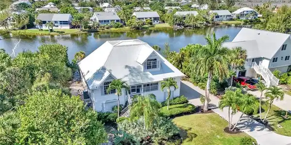 Image 2: Waterfront property featuring a metal roof, mature tropical landscaping, a private driveway, and a waterside patio area