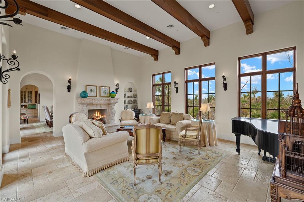 Image 4: Living room with beam ceiling, stone tile flooring, a high end fireplace, arched walkways, and a towering ceiling
