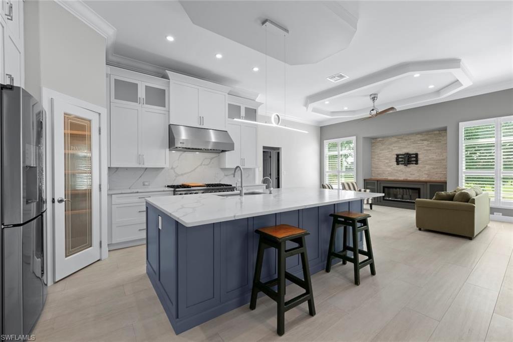Image 2: Modern kitchen featuring a large island with white countertops and a blue base, stainless steel appliances, and white cabinetry