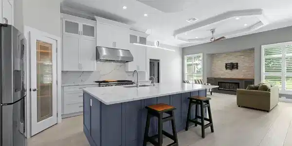 Image 2: Modern kitchen featuring a large island with white countertops and a blue base, stainless steel appliances, and white cabinetry
