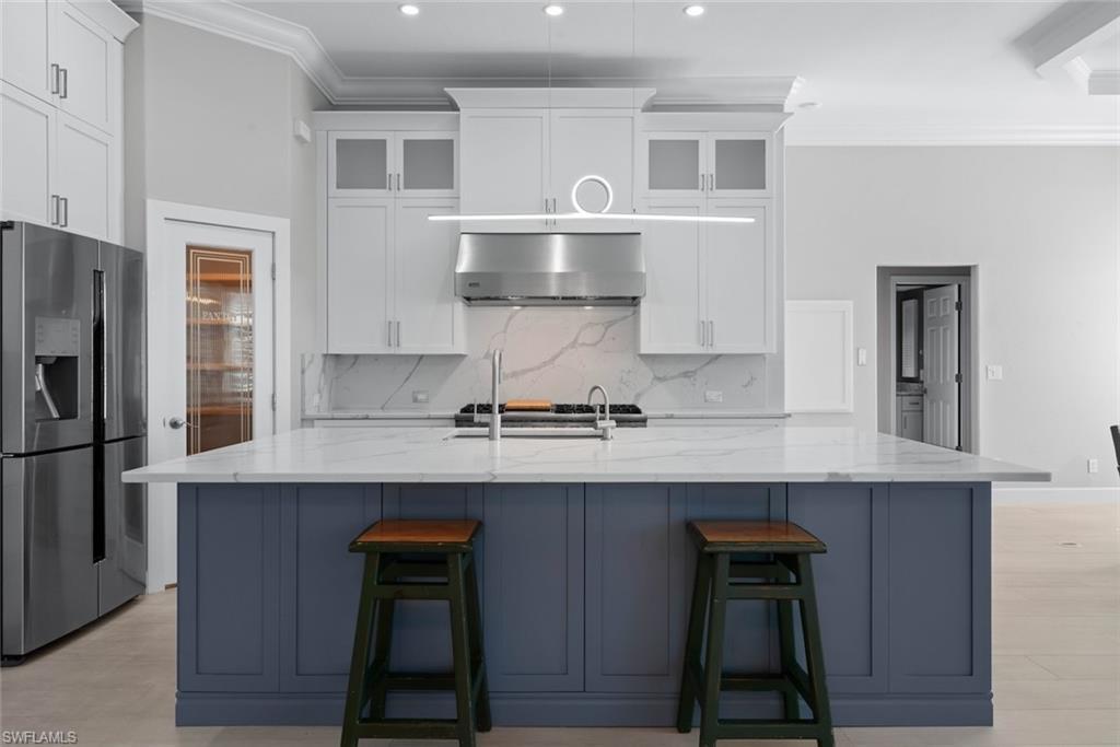 Image 3: Gourmet kitchen featuring a large central island with a quartz countertop, stainless steel appliances, white cabinetry with glass inserts, and a decorative pendant light fixture