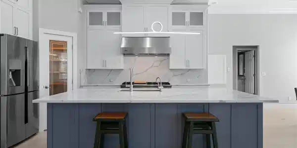 Image 3: Gourmet kitchen featuring a large central island with a quartz countertop, stainless steel appliances, white cabinetry with glass inserts, and a decorative pendant light fixture