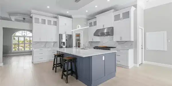 Image 4: Contemporary kitchen featuring a large central island, light wood-finish flooring, white upper and lower cabinetry, stainless steel appliances, and a tray ceiling