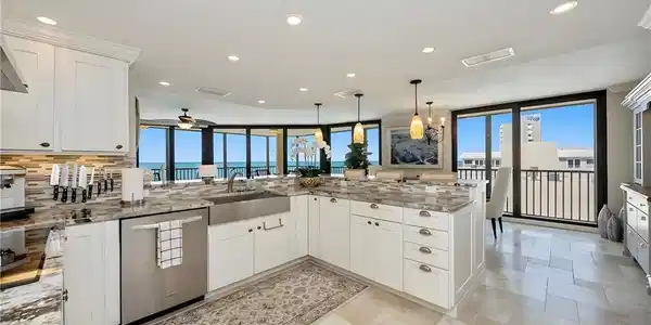 Image 2: Kitchen with white cabinets, a peninsula, light stone countertops, stainless steel dishwasher, and decorative light fixtures