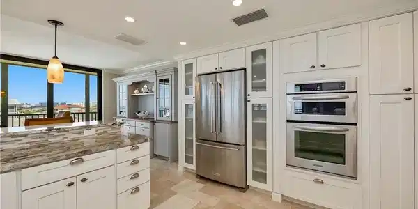 Image 3: Kitchen with white cabinetry, pendant lighting, stainless steel appliances, glass fronted cabinets, and dark stone countertops