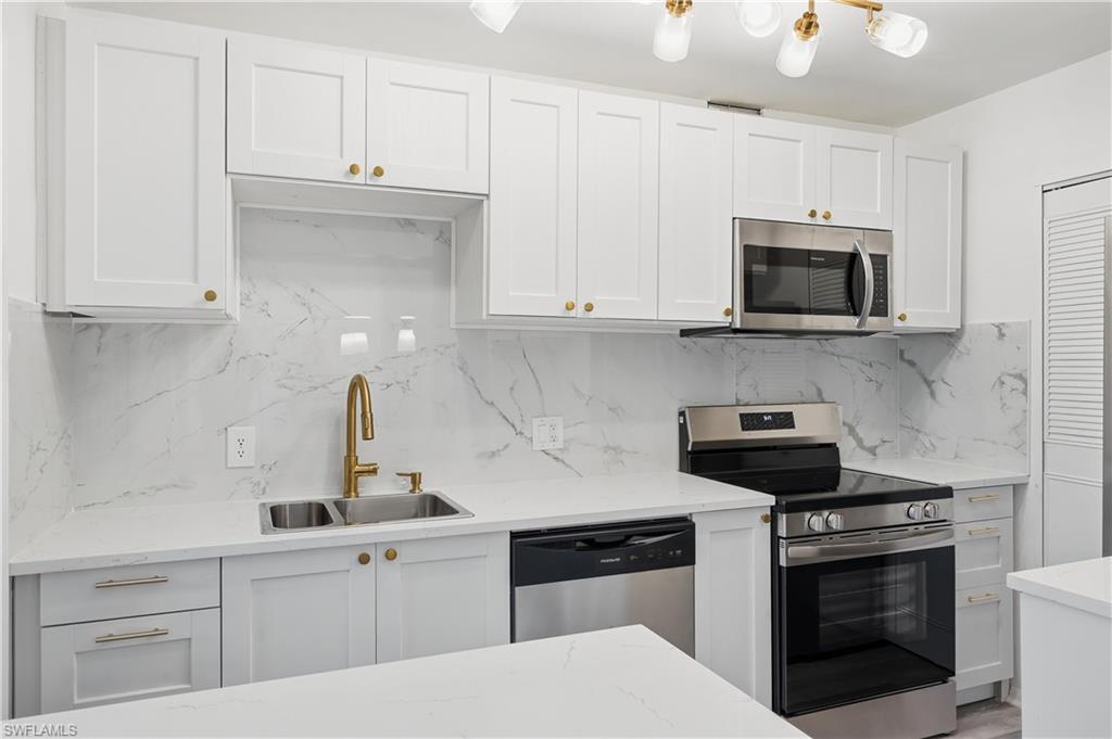 Image 3: Kitchen with stainless steel appliances, white cabinets, light stone counters, and backsplash