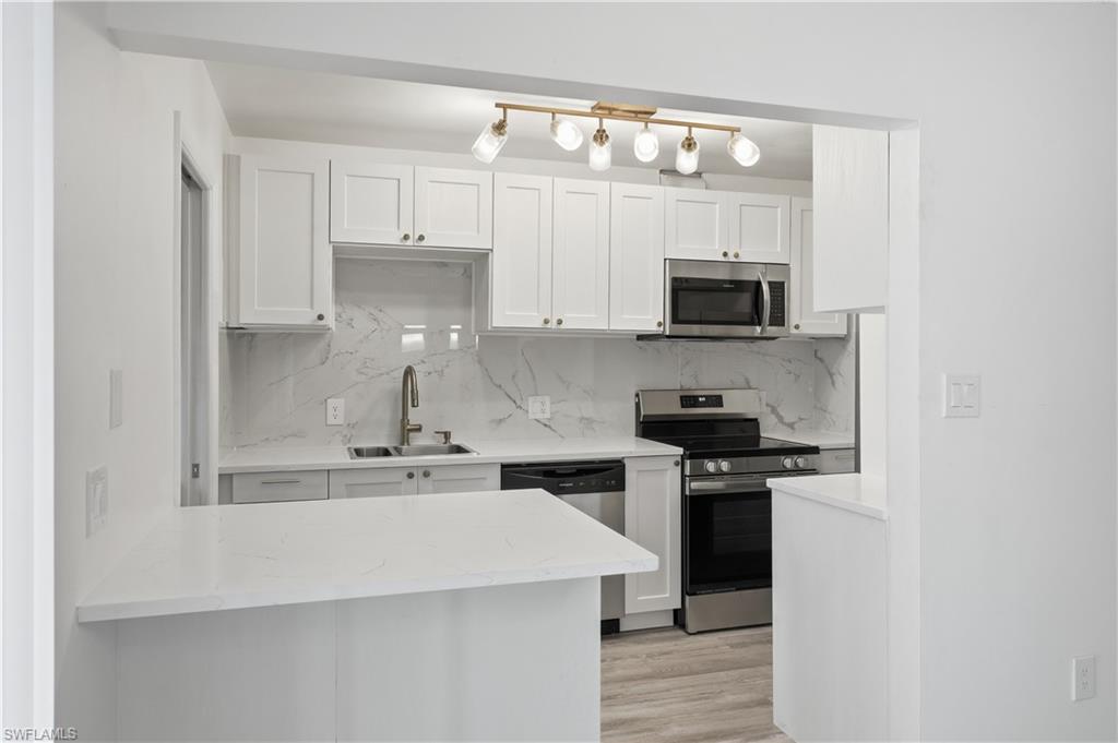 Image 4: Kitchen with stainless steel appliances, white cabinetry, light wood-type flooring, and backsplash