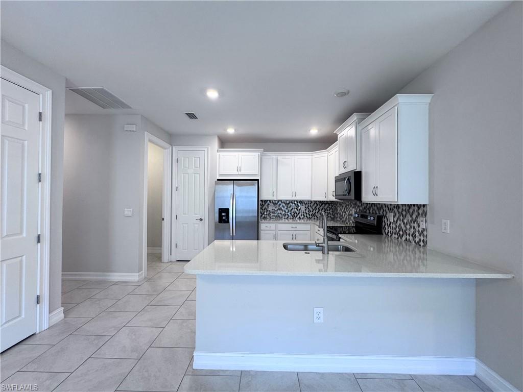 Image 4: Kitchen featuring white cabinetry, light stone counters, stainless steel appliances, decorative backsplash, and light tile patterned floors