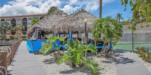 Image 3: Thatched-roof bar structure with blue accents, surrounded by decorative landscaping and gravel