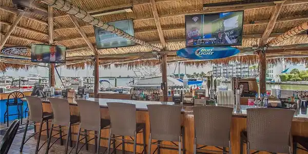 Image 4: Tiki-style bar featuring a thatched roof, wood-finish flooring, and multiple mounted televisions