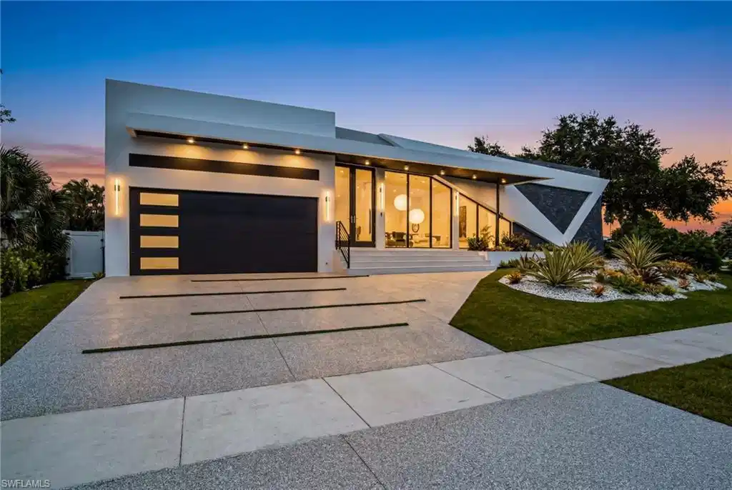 Image 1: Modern architectural exterior featuring a distinct angular design, expansive glass paneling, a two-car garage with frosted glass inserts, a decorative stone facade, and a meticulously landscaped front yard with white stone accents