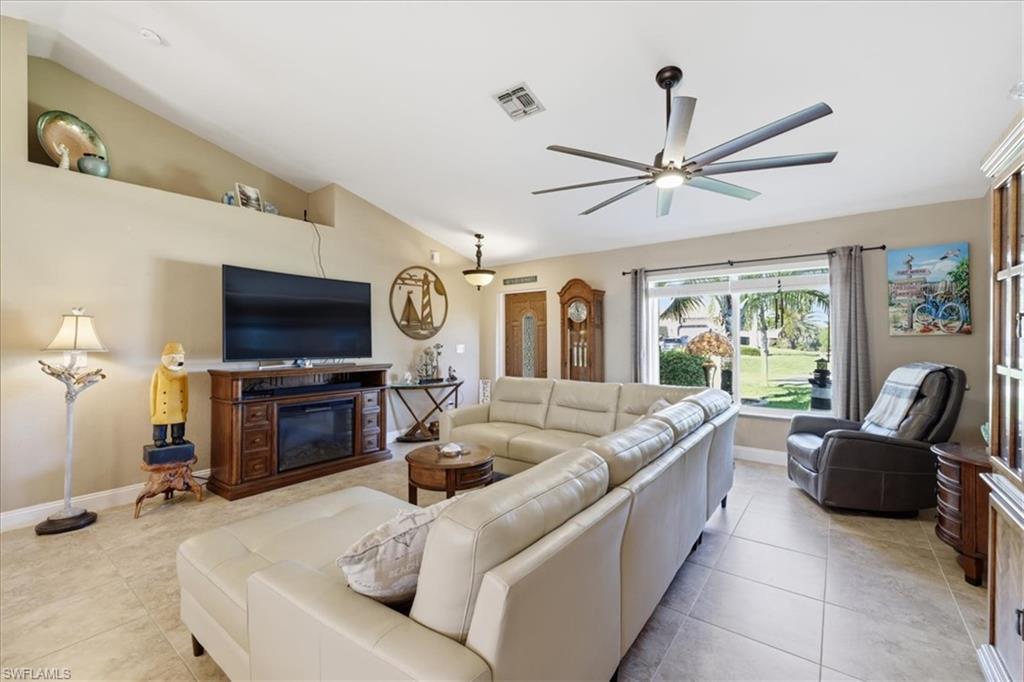 Image 3: Living area featuring lofted ceiling, a ceiling fan, light tile patterned flooring, and a glass covered fireplace