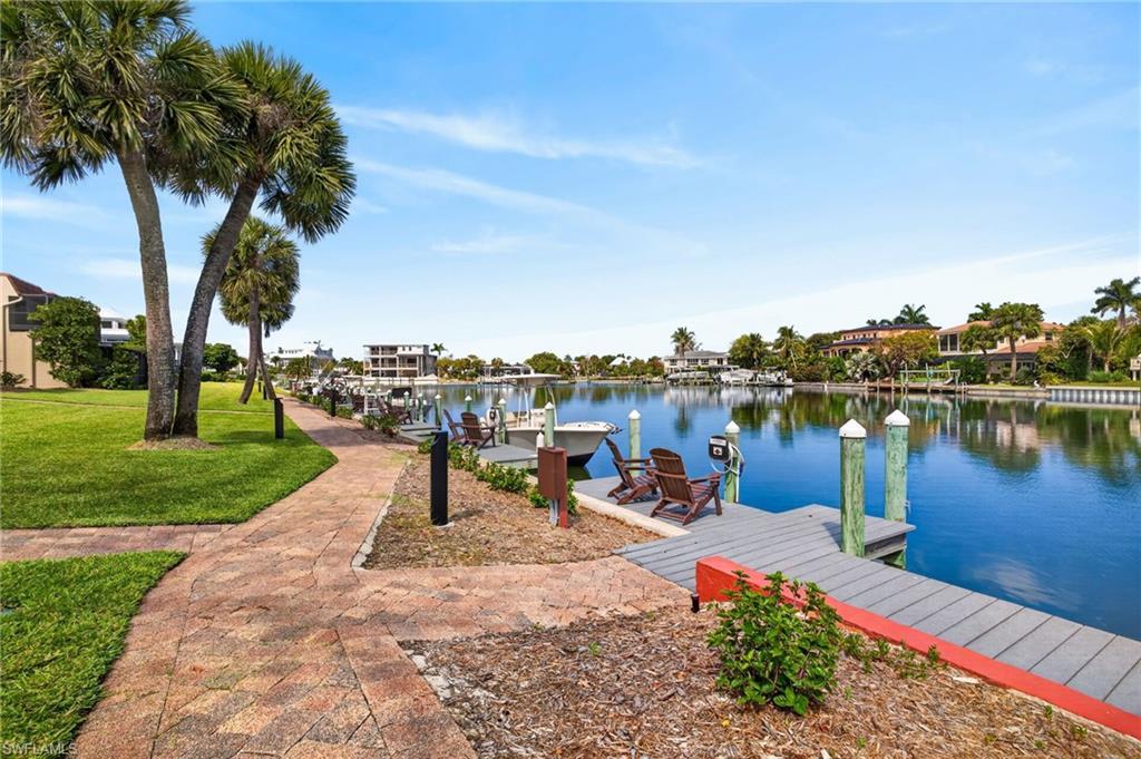 Image 3: Waterfront property featuring a community dock with pilings, a paved pedestrian pathway, and mature palm trees