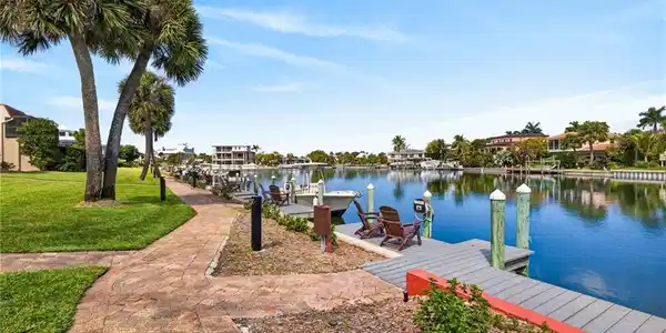 Image 3: Waterfront property featuring a community dock with pilings, a paved pedestrian pathway, and mature palm trees