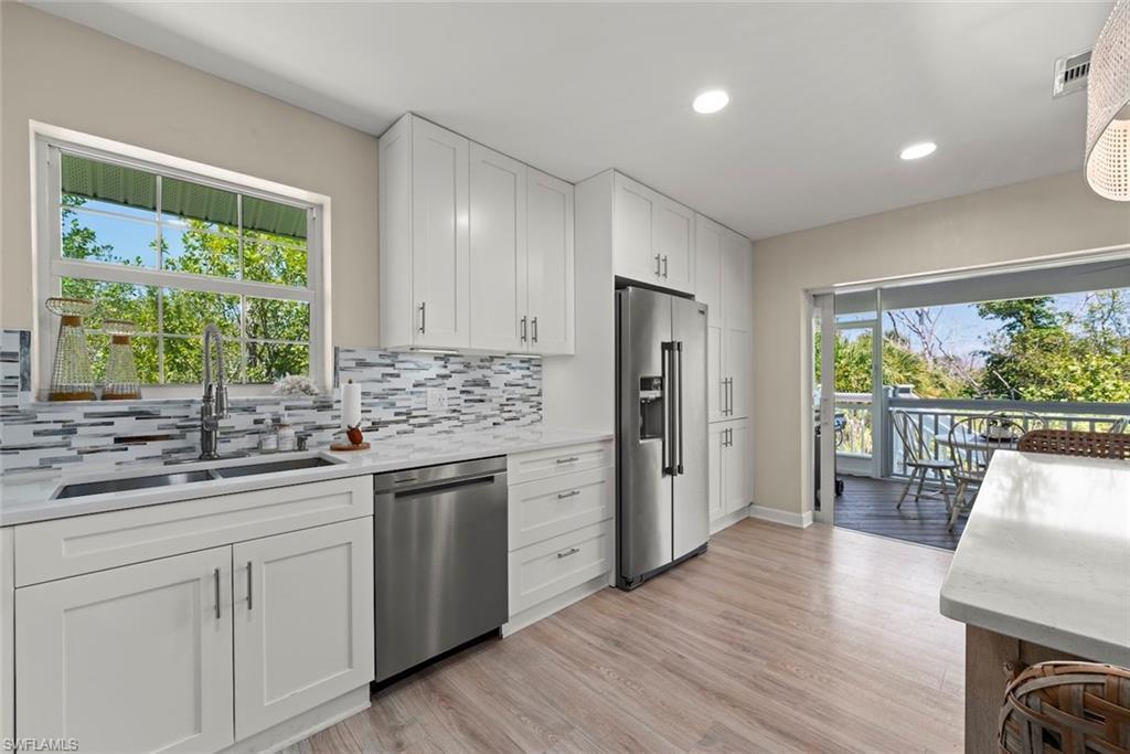 Image 4: Modern kitchen featuring white shaker cabinetry, stainless steel appliances, a mosaic tile backsplash, and wood-finish flooring