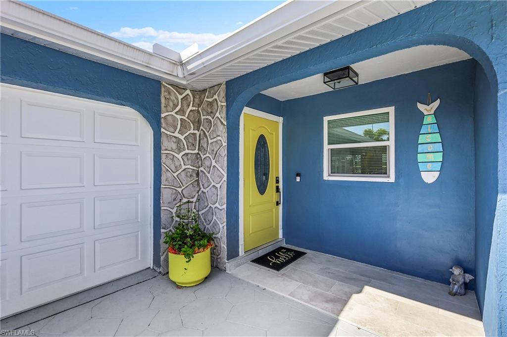 Image 4: Vibrant blue stucco exterior featuring a sunny yellow front door with an oval glass insert, a panel garage door, a stone veneer accent wall, and a patterned concrete entry pad