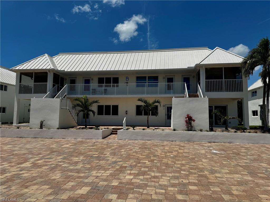 Image 3: Multi-level residence featuring a white metal roof, screened balconies, and ground-level patios