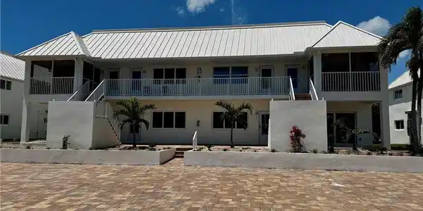 Image 3: Multi-level residence featuring a white metal roof, screened balconies, and ground-level patios