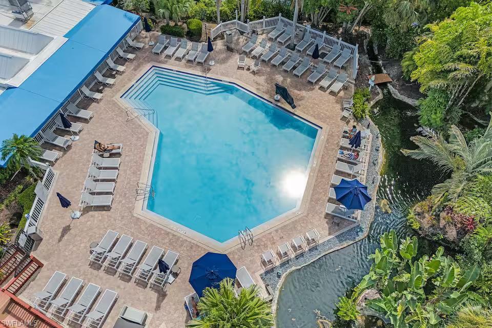 Image 4: The property features an expansive outdoor pool with ample lounge seating and umbrellas, set within a paved patio area