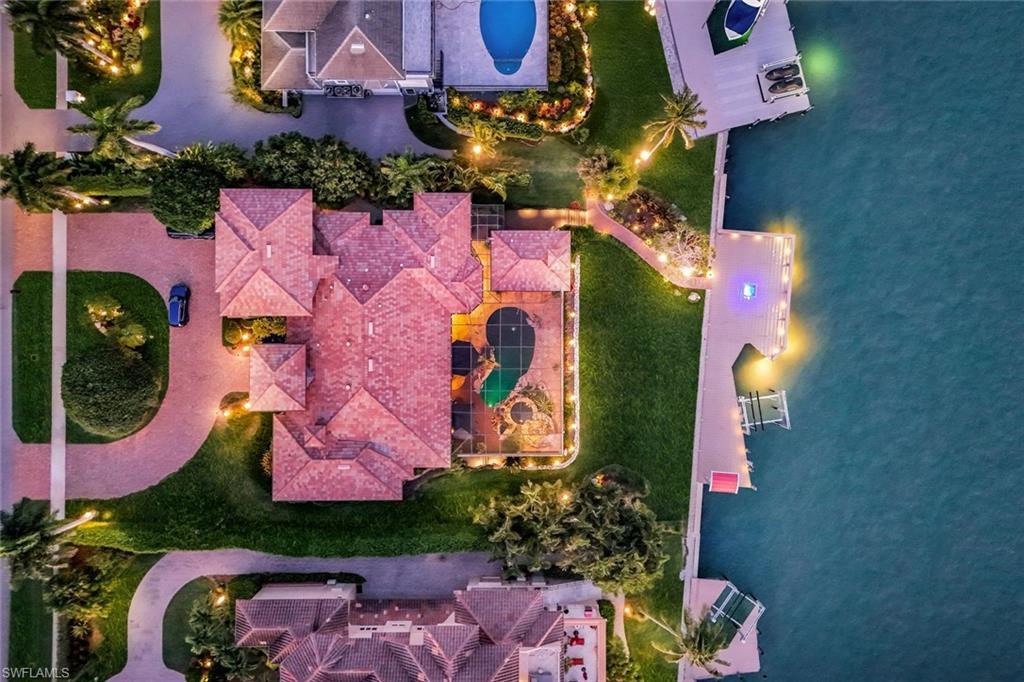 Image 2: Spacious property featuring a multi-gabled tile roof, a custom-shaped swimming pool, expansive waterfront access, a private dock, and manicured landscaping with exterior lighting