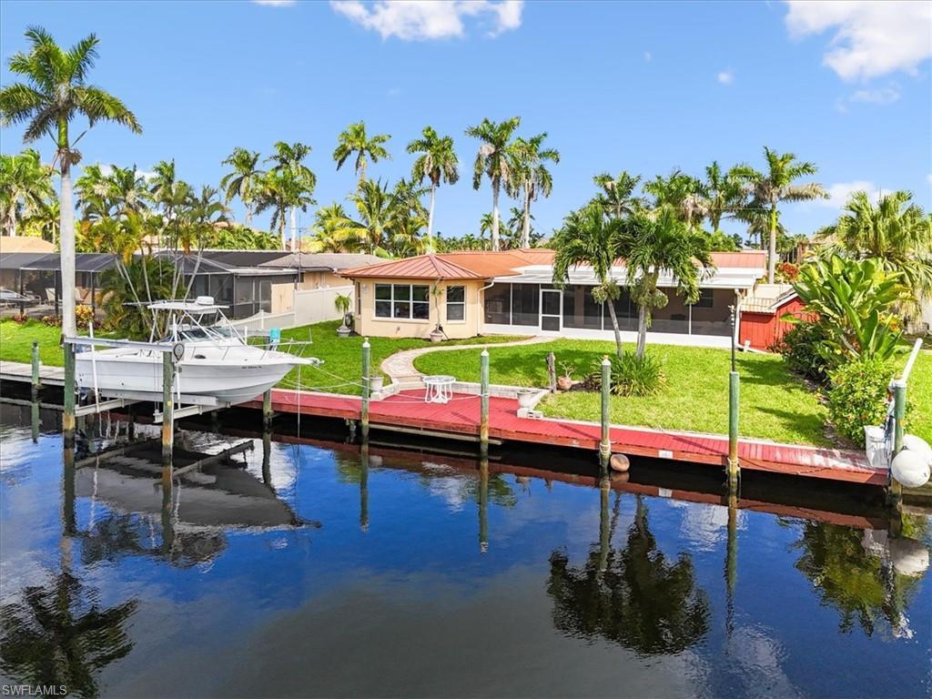 Image 2: Dock featuring a sunroom, boat lift, a lawn, and a water view