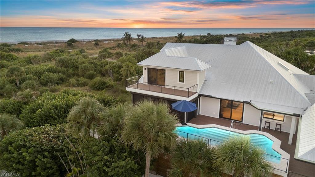 Image 1: Back of property at dusk featuring a balcony, an outdoor pool, a metal roof, a chimney, and a water view