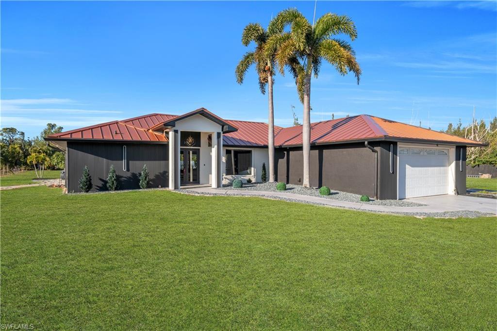 Image 1: View of front of house featuring a front lawn, a metal roof, a garage, and concrete driveway