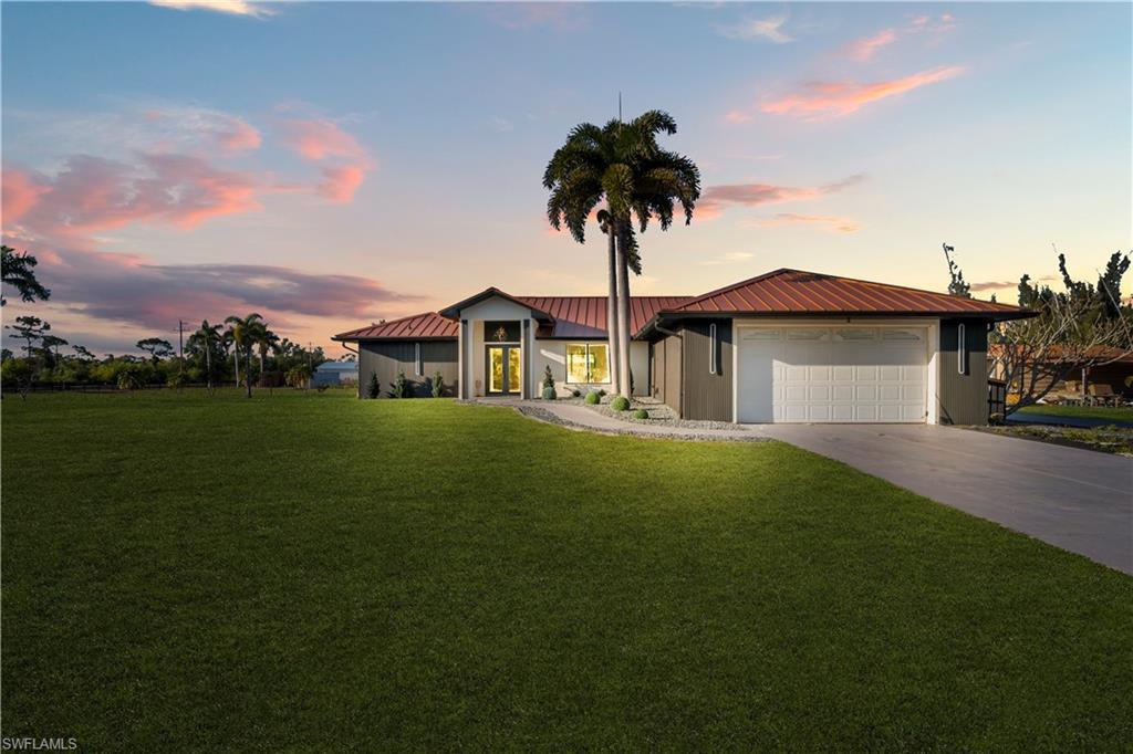 Image 3: View of front of home with a front yard, driveway, a metal roof, and a garage
