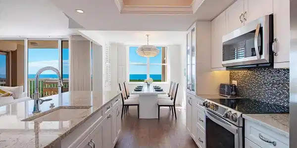 Image 4: Kitchen with stainless steel appliances, a tray ceiling, white cabinets, light stone countertops, and hanging light fixtures