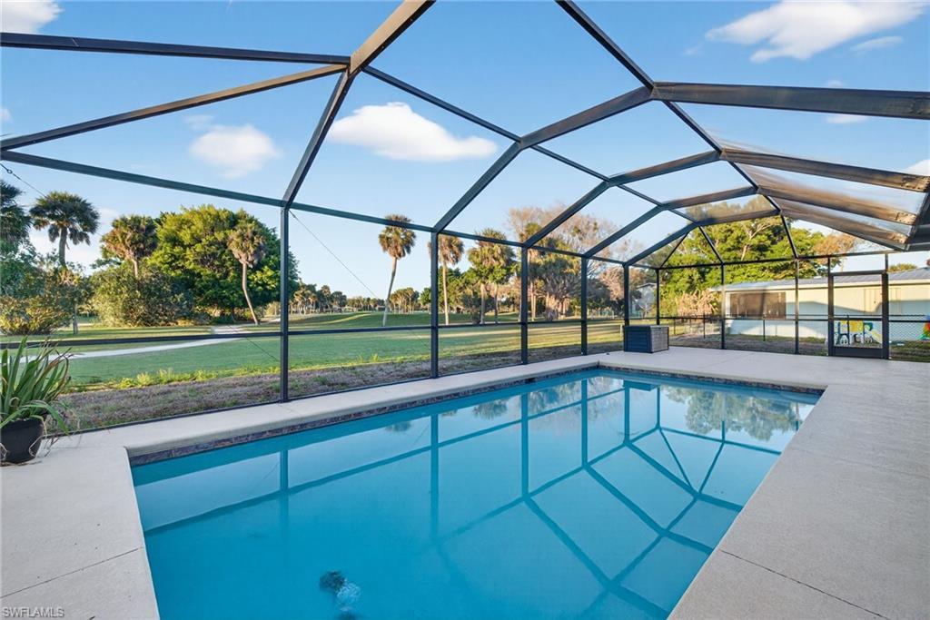 Image 1: Screened-in pool deck featuring a geometric-shaped swimming pool with a tiled edge, concrete pool deck, and a transparent screen enclosure