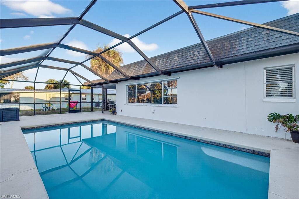 Image 3: Screened outdoor pool with a dark blue tile border, light-colored pool deck, and white stucco exterior wall