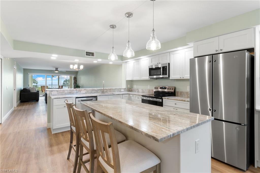 Image 2: Kitchen featuring stainless steel appliances, open floor plan, a breakfast bar area, white cabinetry, and light wood-style floors