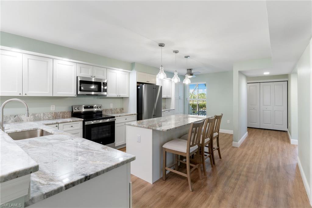 Image 3: Kitchen with appliances with stainless steel finishes, pendant lighting, a kitchen bar, light stone countertops, and a center island